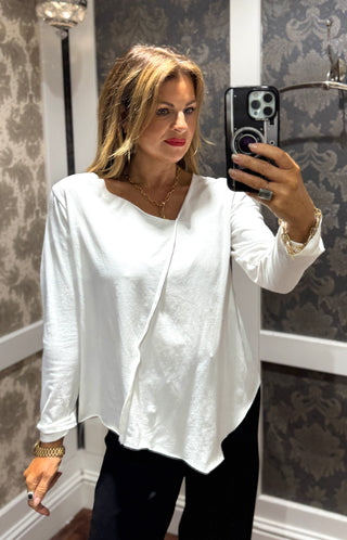 This white long sleeve top features stylish 3/4 length cuffed sleeves for a polished touch. The asymmetrical neckline and hem create a modern silhouette, while the stitch detail across the front adds unique character. Perfect for those who appreciate subtle, distinctive design that sets you apart effortlessly.